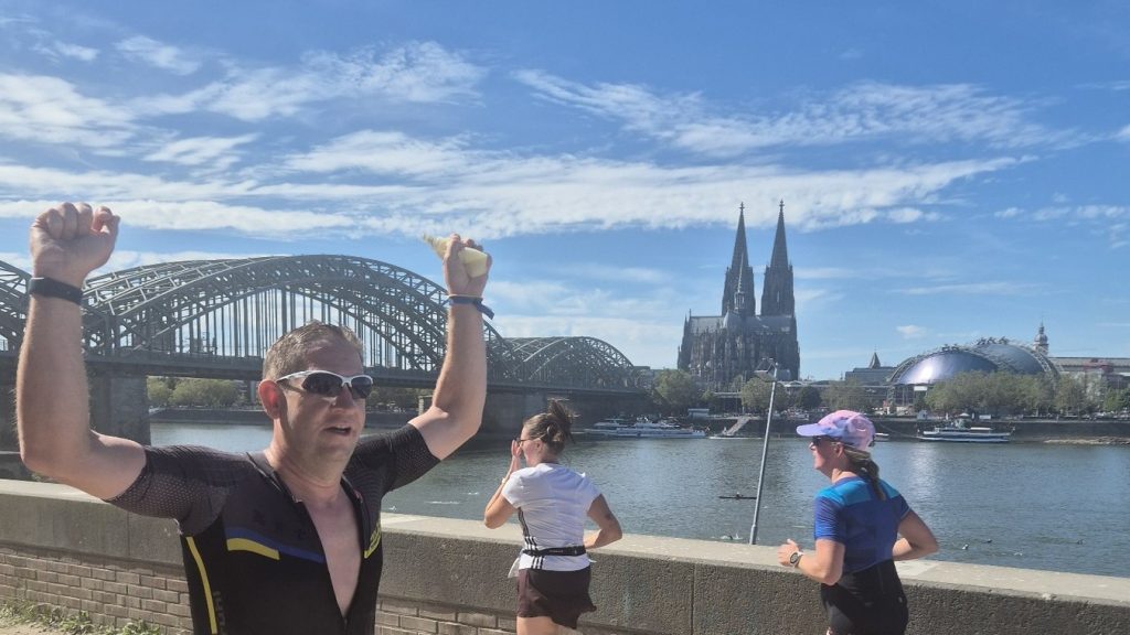 Mirco Hübner vom PSV Brühl Triathlon Team mit Startnummer 2312 beim Laufen am Rheinufer, im Hintergrund Hohenzollernbrücke und Kölner Dom
