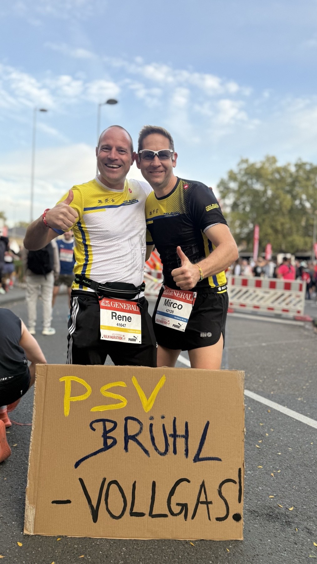 Rene Kramer mit Startnummer 41647 und Mirco Hübner mit Startnummer 43128 in PSV-Trikots mit Daumen hoch hinter einem Schild mit der Aufschrift PSV Brühl Vollgas