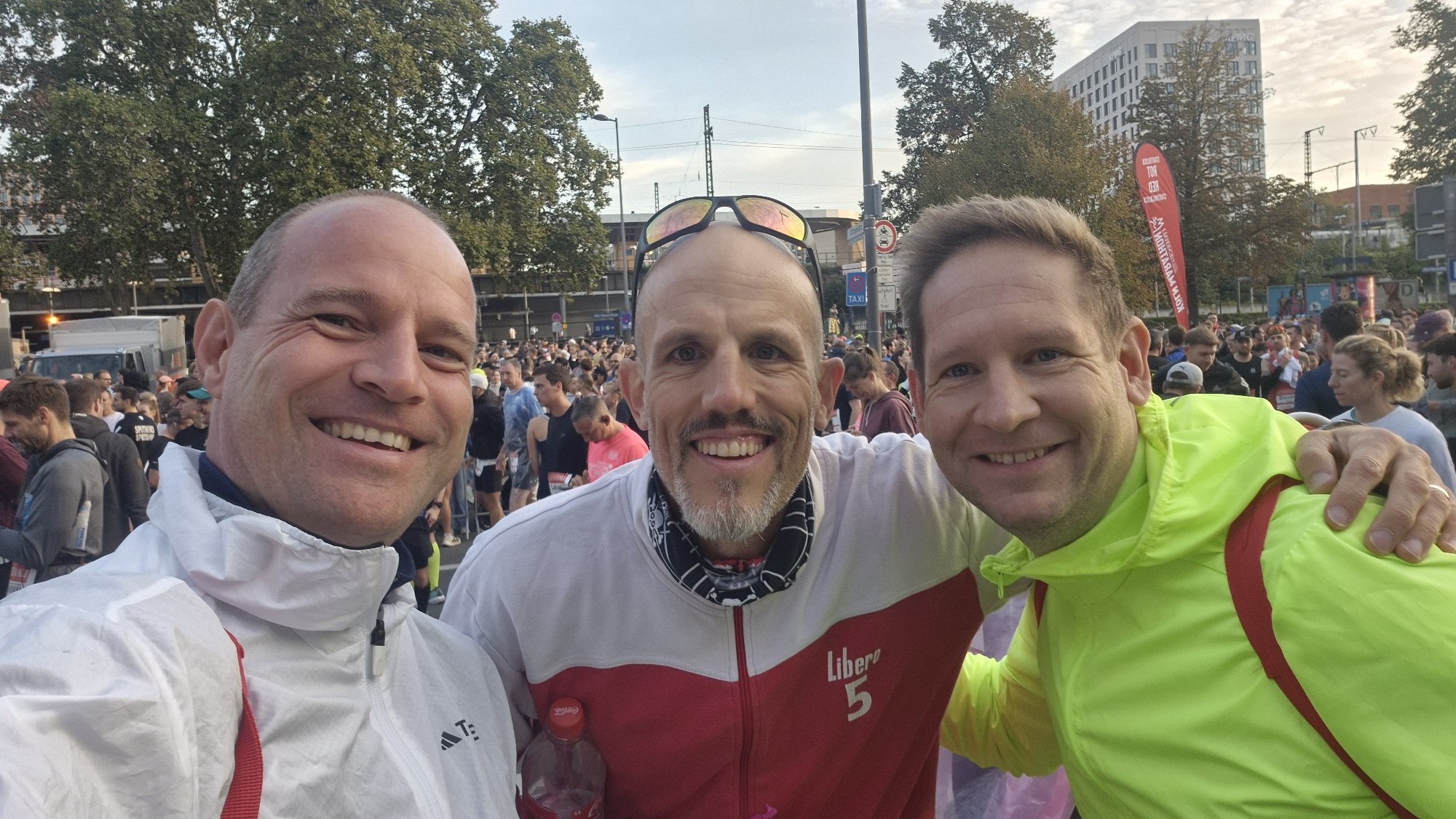 Drei Läufer im Startbereich des Generali Köln Marathon 2026, hinter ihnen dicht gedrängt das Läuferfeld