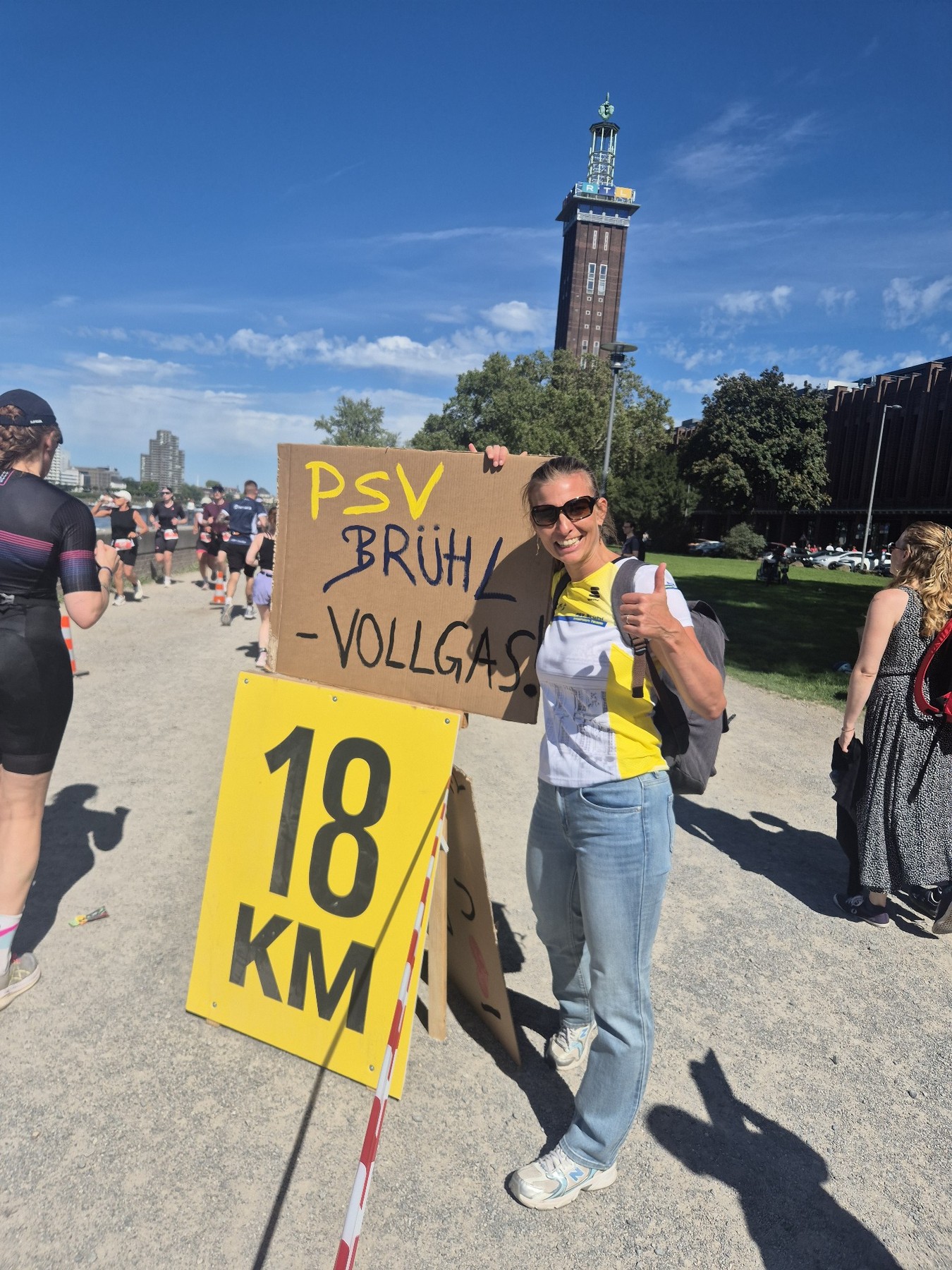 Frau im gelb-weißen PSV-Trikot hält am Streckenrand ein selbst gemaltes Schild mit der Aufschrift PSV Brühl Vollgas