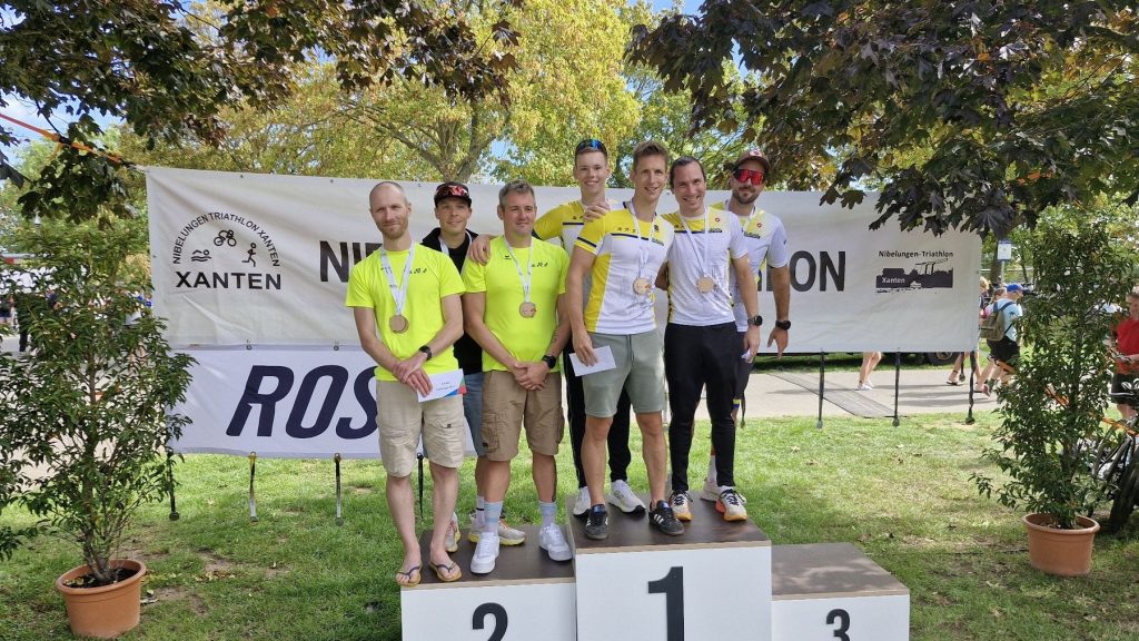 Sportler mit Medaillen bei der Siegerehrung des 40. Nibelungen Triathlon in Xanten vor dem Banner mit dem Veranstaltungsnamen