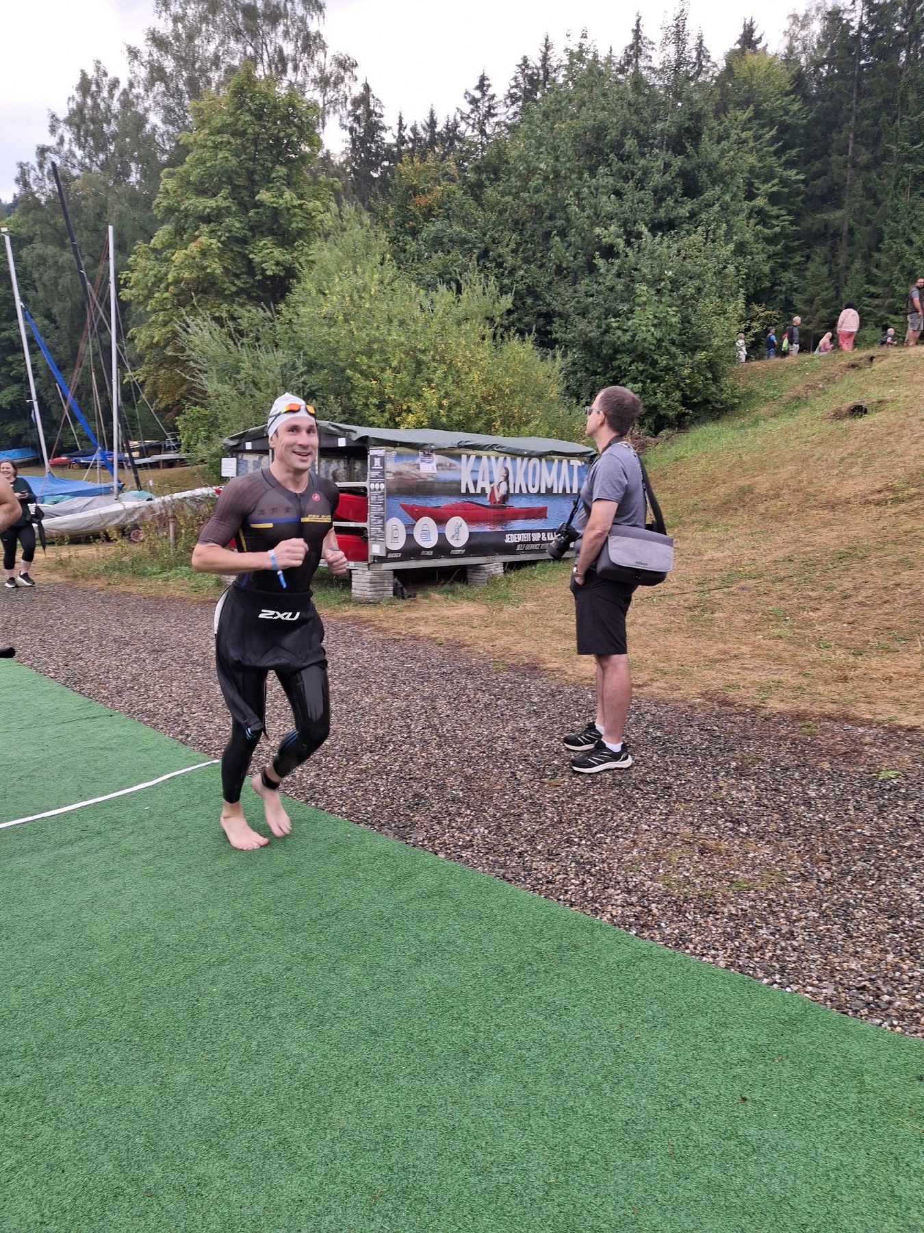 Björn Zeese vom PSV Brühl Triathlon Team im Neoprenanzug läuft barfuß über die grüne Matte zum Schwimmstart des Nordschwarzwald Triathlon