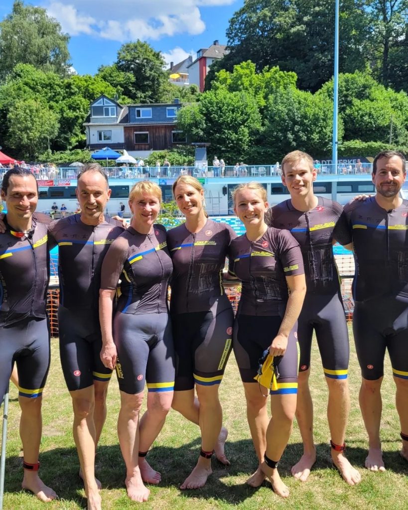 Gruppenfoto des PSV Brühl Triathlon Team in schwarzen Trikots mit gelb-blauen Streifen am Seeufer nach dem Stadtwerke Bochum Triathlon 2026